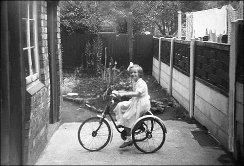 Photograph showing Sue at home on her tricycle